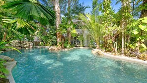 Una piscina cristalina rodeada de vegetación tropical y un muro de piedra.