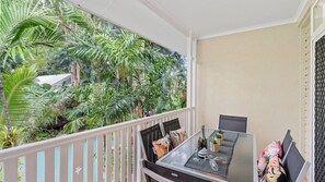 A balcony with a table set for dining, surrounded by lush tropical plants.
