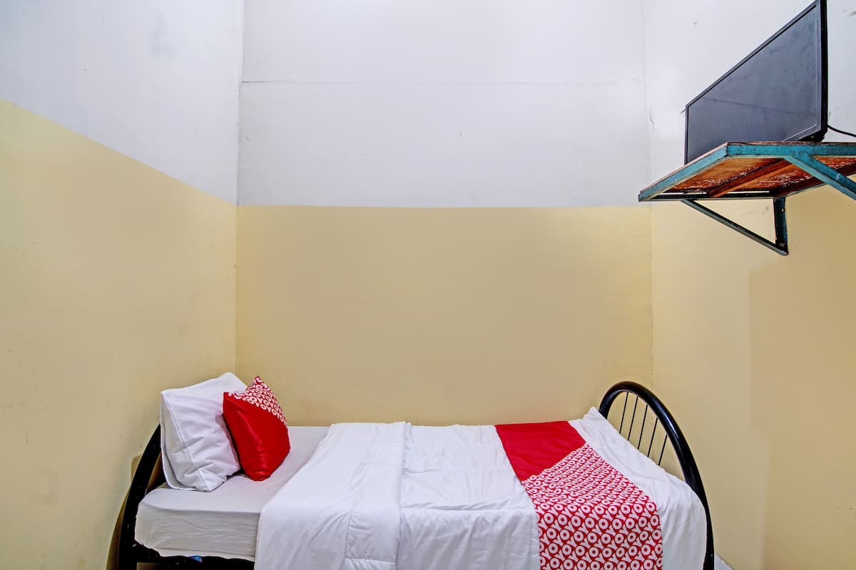 A small, single-bed room with a white and red bedspread, a red pillow, and a black metal headboard.
