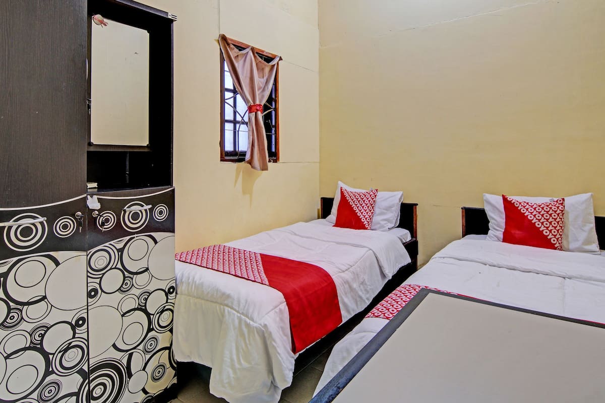 A hotel room with two beds, a large mirror, a window with curtains, and a patterned wardrobe.