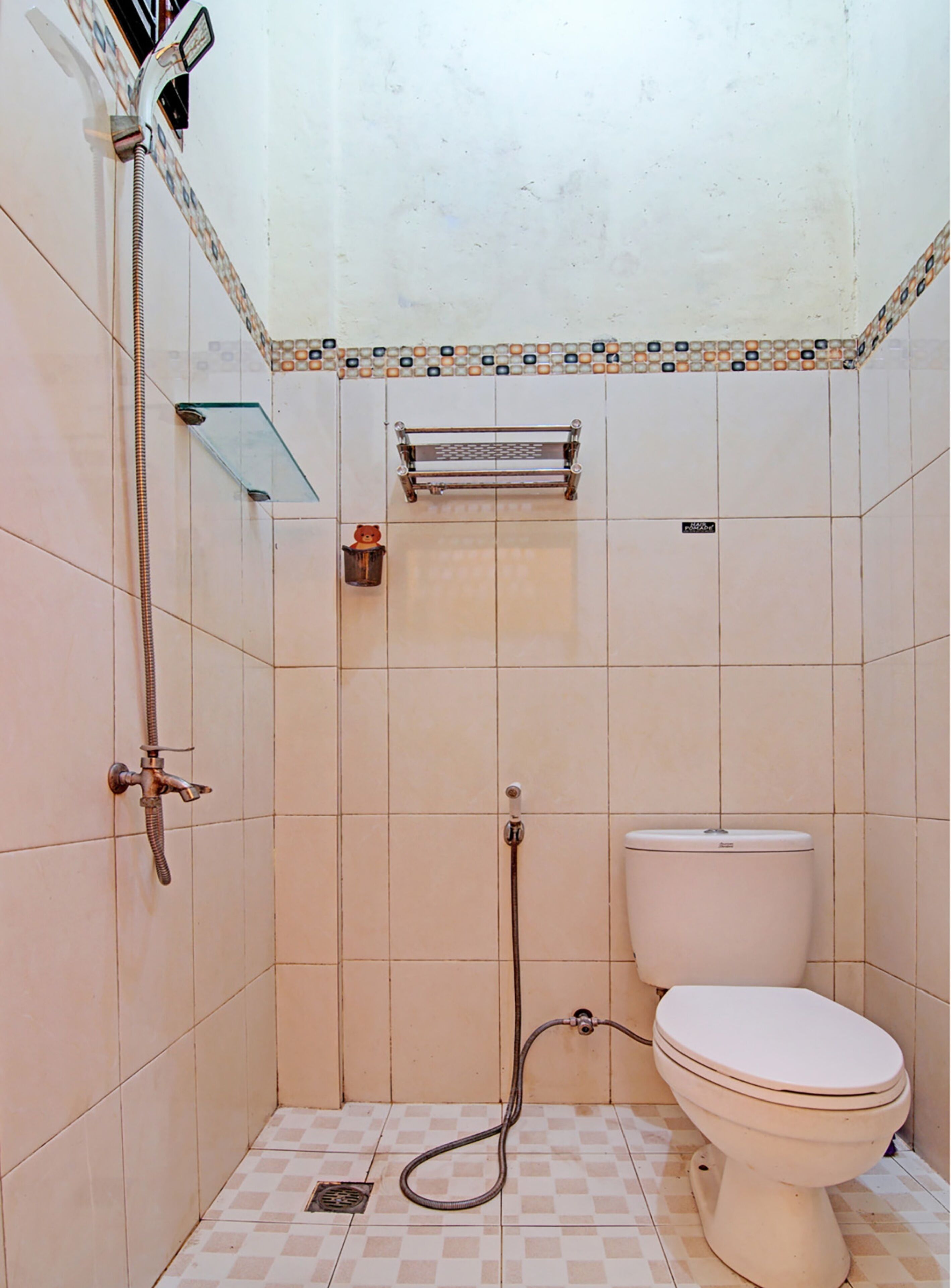 Une petite salle de bain carrelée, équipée d’une douche, de toilettes et d’une étagère en verre.