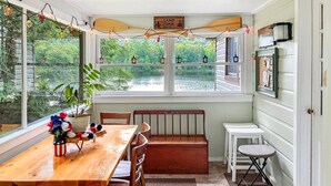 Un comedor acogedor con una mesa y sillas de madera, un banco y vistas a un lago a través de amplios ventanales.