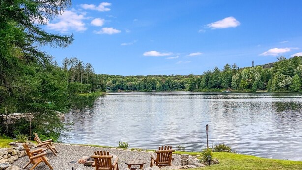 Un entorno junto al lago con zona de grava, sillas de madera tipo Adirondack y una pequeña mesa.