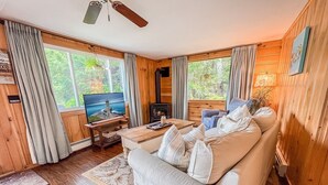 Una sala de estar acogedora con sofá, televisor, chimenea y ventanas amplias con cortinas.
