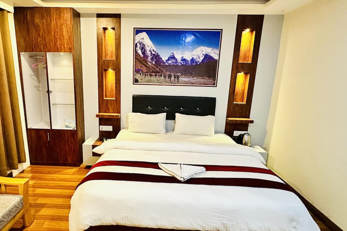 A hotel room with a large bed, a wooden wardrobe, a desk, and a chair.