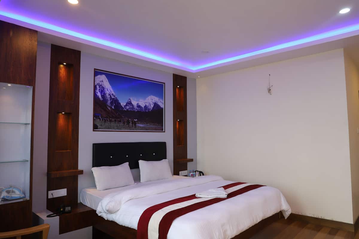 A hotel room with a large bed, a mounted picture of a mountain, and a wooden nightstand with a phone.