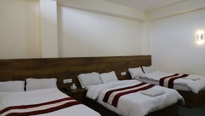 A hotel room with three beds, each with white bedding and red accents, a wooden headboard, and a small bedside table with a lamp. - Hotel Pyarij Taplejung (Taplejung)