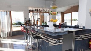 A modern bar area with a marble countertop, bar stools, and a variety of bottles and glasses. - Ledras Beach Hotel (Rhodes)