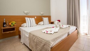 A hotel room with a bed, a nightstand with a bottle and fruit, and a window with curtains. - Ledras Beach Hotel (Rhodes)