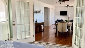 A room with a bed, a dining area with a table and chairs, and a kitchen area with a TV. - GOTL Strip - Private Beach - Lake Erie Views- Sunset Vacation Rentals (Geneva)