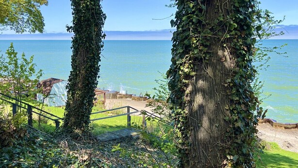 A view of a lake with a wooden staircase leading down to a grassy area. - GOTL Strip - Private Beach - Lake Erie Views- Sunset Vacation Rentals (Geneva)