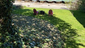 A grassy area with two Adirondack chairs facing a calm sea, a concrete breakwater, and a clear sky. - GOTL Strip - Private Beach - Lake Erie Views- Sunset Vacation Rentals (Geneva)