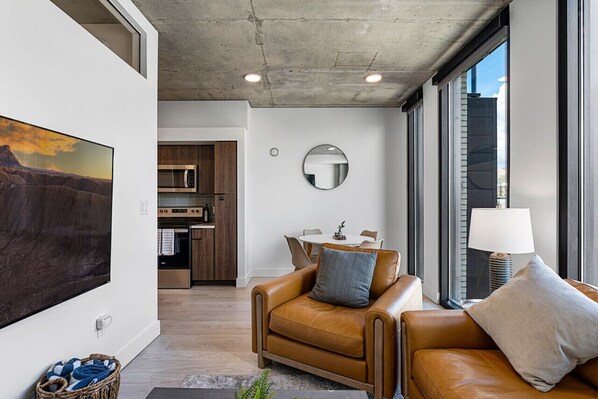 A modern living room with a leather sofa, a flat-screen TV, and a dining area with a table and chairs.