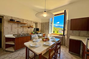 A modern kitchen with a dining area, equipped with a stove, sink, and a large window offering a scenic view. - Villa Near Golf Club Menaggio (Grandola ed Uniti)