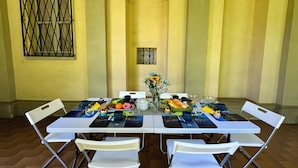 Uma mesa de jantar posta com cadeiras, um vaso de flores e diversos alimentos.