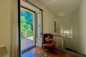 A room with a sliding glass door leading to a balcony, a wooden chair with a floral cushion, and a staircase with a white railing.