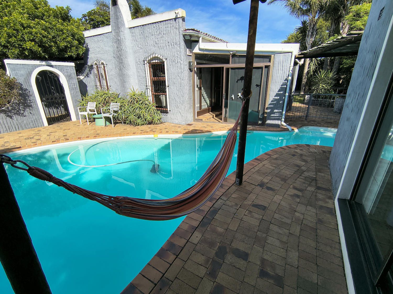 A swimming pool with a hammock, a brick patio, and a building with a unique architectural style.