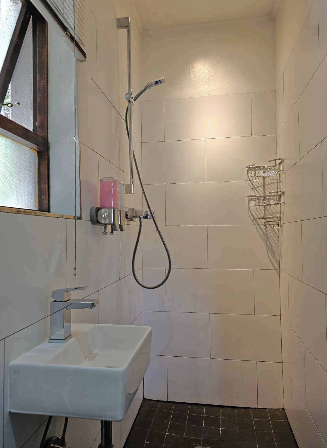 Un bagno piccolo rivestito di piastrelle, con un lavandino bianco, una doccia con soffione a mano e un mobiletto a mensole in metallo.