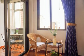 A room with a wicker chair, a small table with a vase, and a view through a glass door. - Beach Breeze · Pool Views · Playa Santiago (CN)