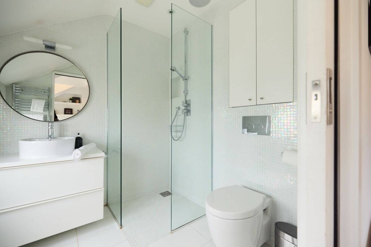 A modern bathroom with a glass-enclosed shower, a round mirror, a white sink, and a toilet.