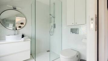 A modern bathroom with a glass-enclosed shower, a round mirror, a white sink, and a toilet.