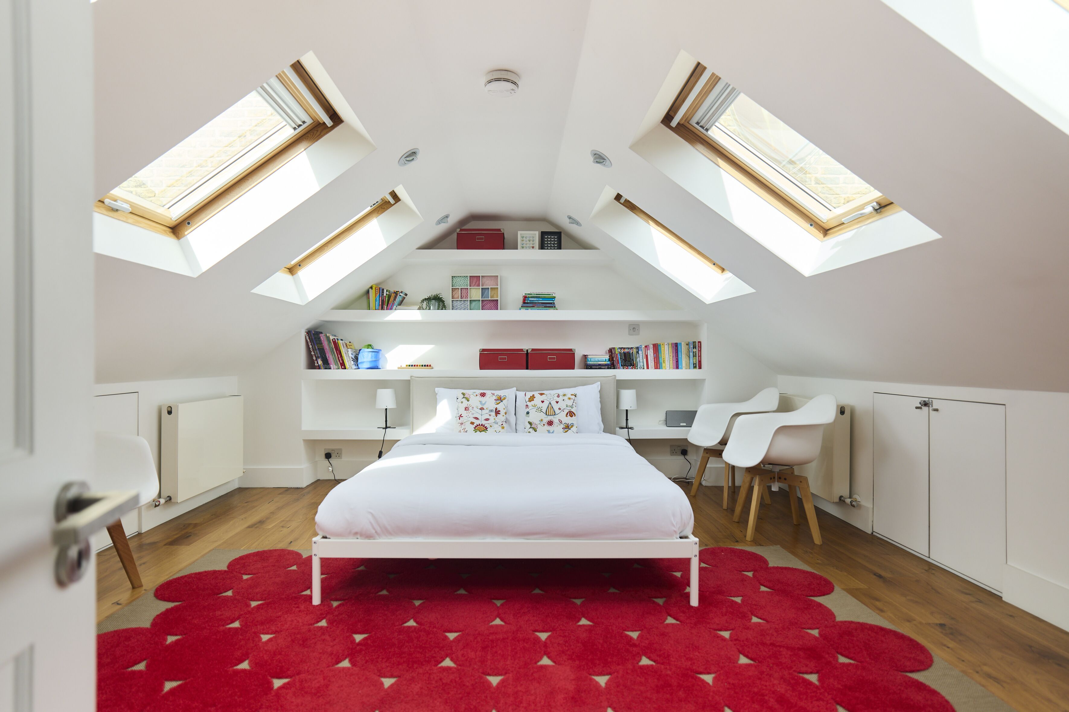 A bedroom with a skylight, a bed, a desk, and bookshelves.