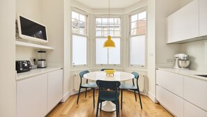 A modern kitchen with white cabinets, a round table, and blue chairs. - The Clapham Crib (London)