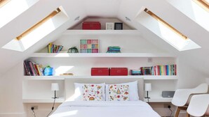 A bedroom with a sloped ceiling, skylights, a bed, bedside tables, a desk, and a chair. - The Clapham Crib (London)