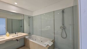 A modern bathroom with a large mirror, a bathtub, a shower area, and a vanity with a sink. - Dorisol IV - Luxury Apartment in La Vie (Funchal)