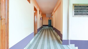 A hallway with a tiled floor, wooden doors, and a window with a metal grille. - Hotel Pine & Dine Almora (Almora)