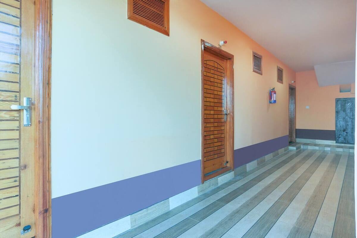 A hallway with a wooden door, a small vent, and a fire extinguisher on the wall.