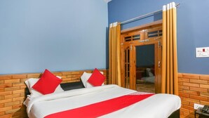 A hotel room with a bed, a wooden headboard, a red and white bedspread, and a wooden door with curtains. - Hotel Pine & Dine Almora (Almora)