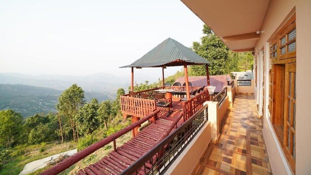 A balcony with a wooden deck, a covered seating area, and a view of the landscape. - Hotel Pine & Dine Almora (Almora)