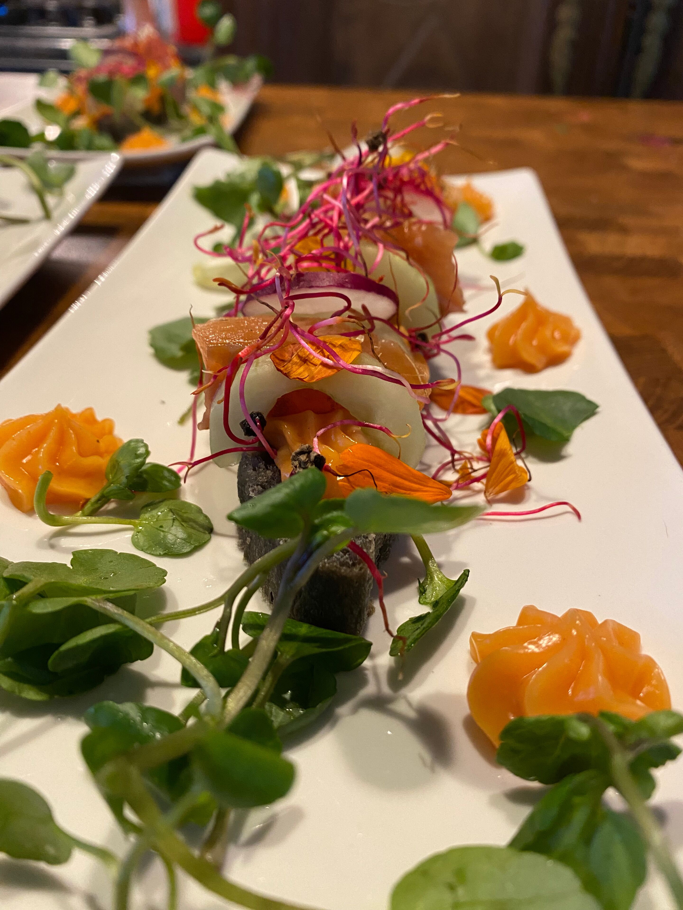A long rectangular table with a white plate containing a dish of food, garnished with green leaves and orange elements.