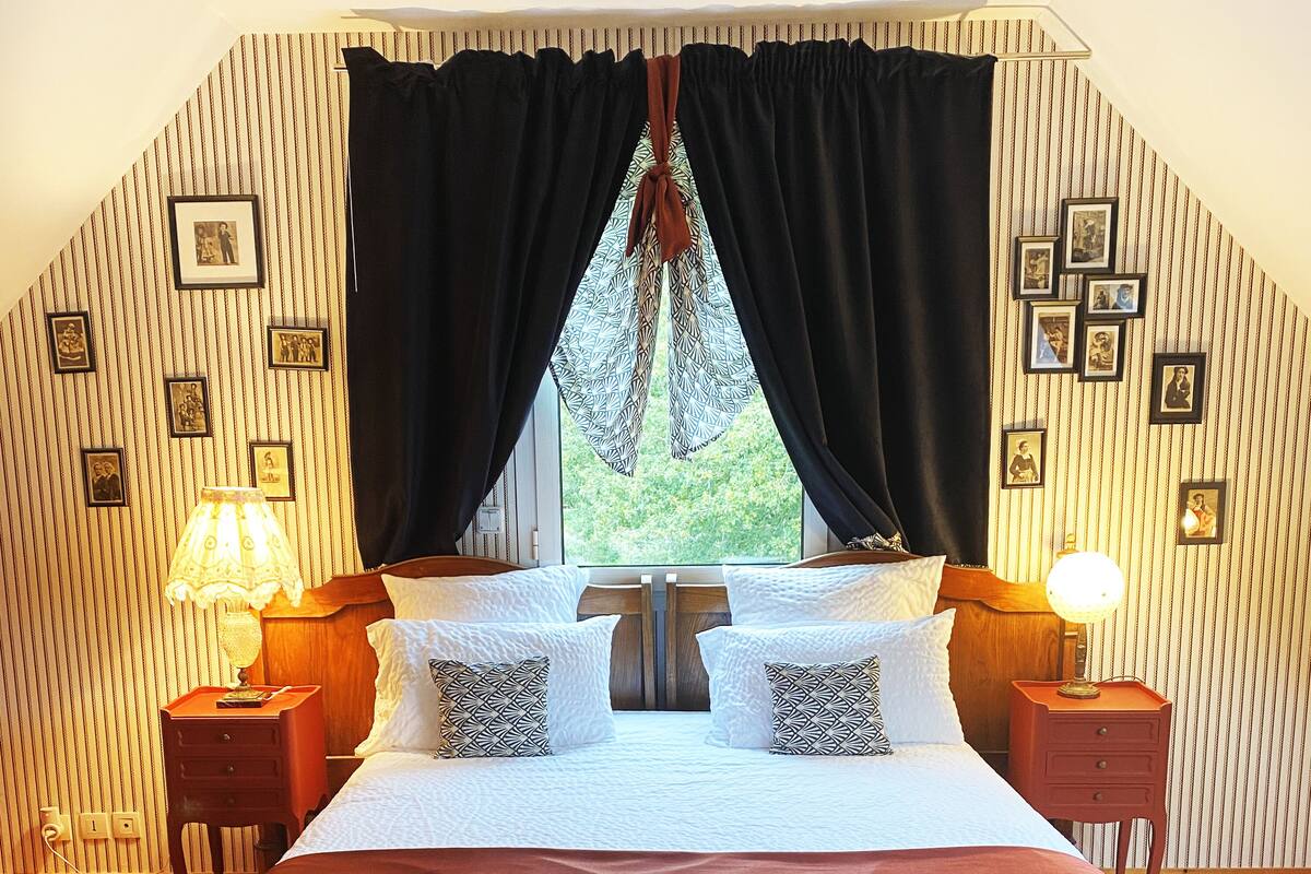 A bedroom with a large bed, two bedside tables with lamps, a bench, and a window with curtains.