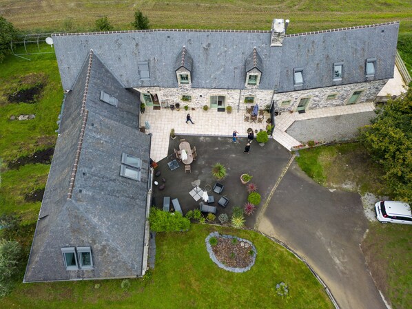 A stone building with a courtyard, outdoor seating, and a car parked nearby. - Les Pierres Bleues (Saint-Coulitz)
