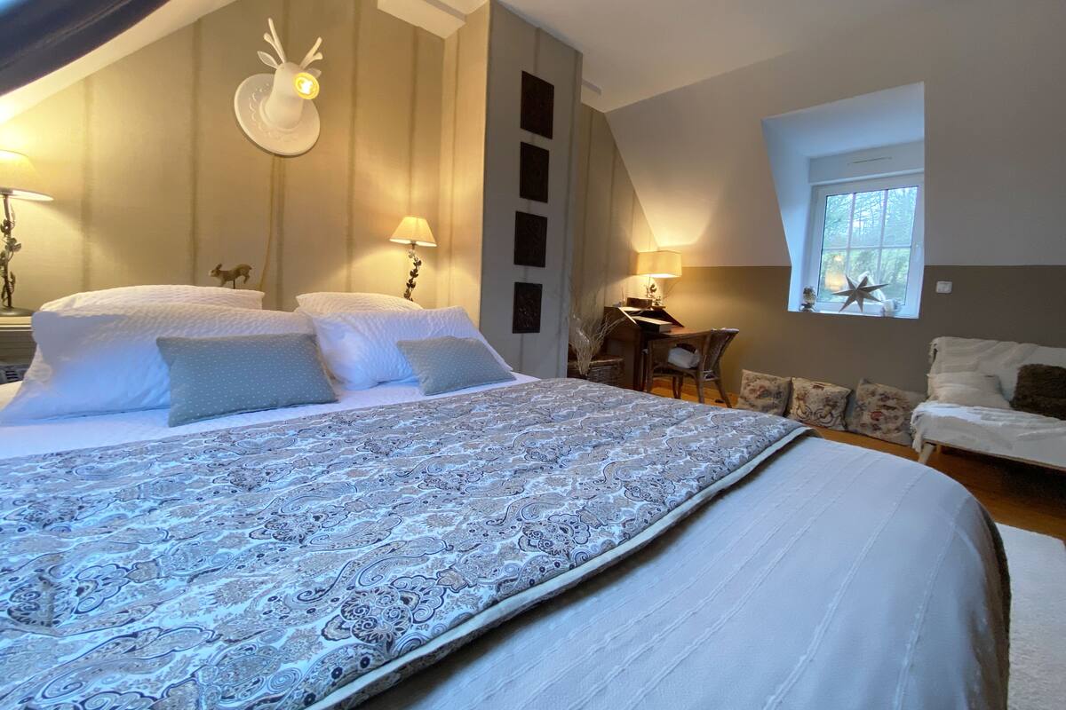 A bedroom with a large bed, two bedside tables with lamps, a small desk, and a window with a star decoration.