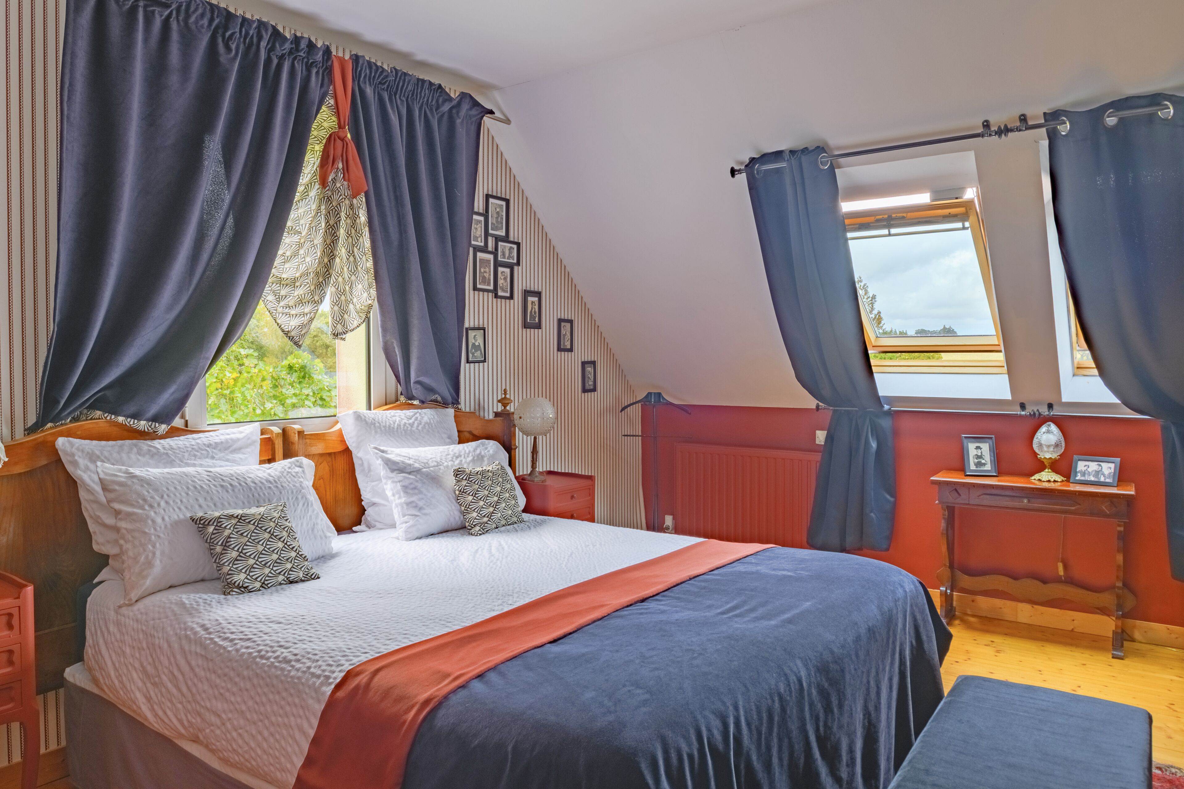 A bedroom with a bed, curtains, a nightstand, a bedside table, and a window with a view.