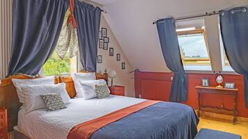 A bedroom with a bed, curtains, a nightstand, a bedside table, and a window with a view.