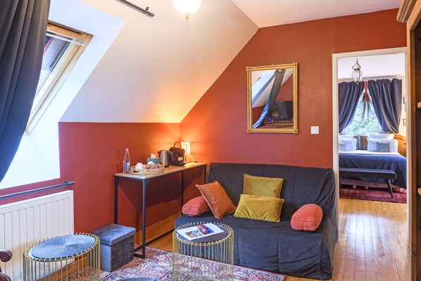 A cozy room with a dark blue sofa, a small round table, and a window with curtains. - Les Pierres Bleues (Saint-Coulitz)