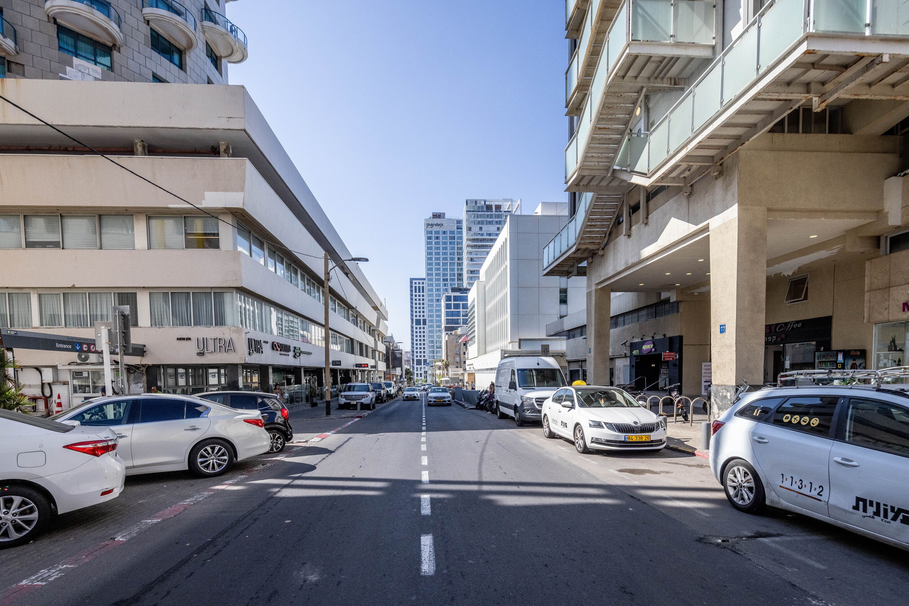 Una strada cittadina con auto parcheggiate, edifici e cielo sereno.