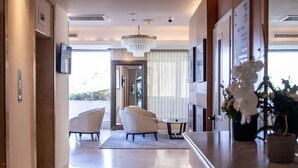 A modern hotel lobby with a marble floor, two armchairs, a round table, a chandelier, and a large window with curtains. - Grand Sea View Retreat by Sea N' Rent (Tel Aviv)
