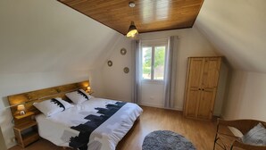 A bedroom with a wooden ceiling, a bed with a patterned bedspread, a wooden wardrobe, a round rug, and a chair with a cushion. - Maison de Campagne Avec Piscine (Rives)