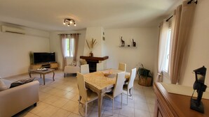A living room with a TV, sofa, and dining area with chairs and a table. - Maison de Campagne Avec Piscine (Rives)