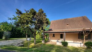 A two-story house with a tiled roof, a covered porch, and a small garden area. - Maison de Campagne Avec Piscine (Rives)