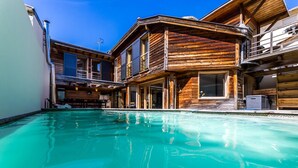 Un área de piscina con edificios de madera, una piscina azul cristalina y un cielo soleado.