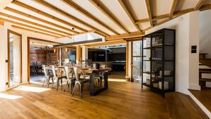 Un amplio comedor con una mesa y sillas de madera, una cocina al fondo y una escalera que sube a otro nivel.
