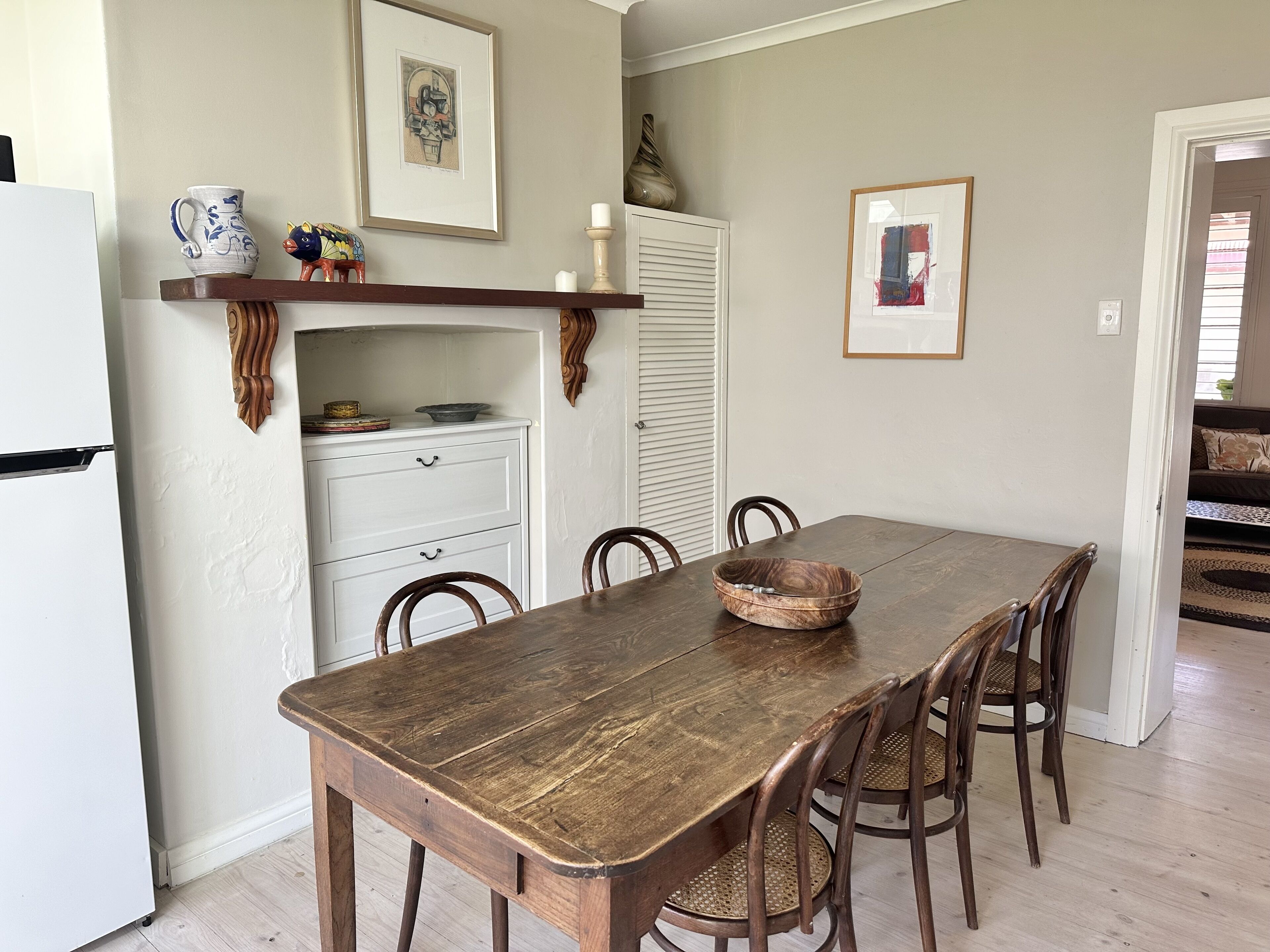 Een eethoek met een houten tafel, stoelen, een wit kastje en decoratieve objecten.
