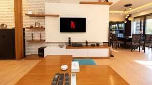 A modern living room with a flat-screen TV mounted on a white brick wall, wooden furniture, and a dining area with a table and chairs. - Prime select Sodic Eastown New Cairo (New Cairo)