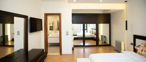 A modern hotel room with a large bed, a TV, a mirror, and a walk-in closet.